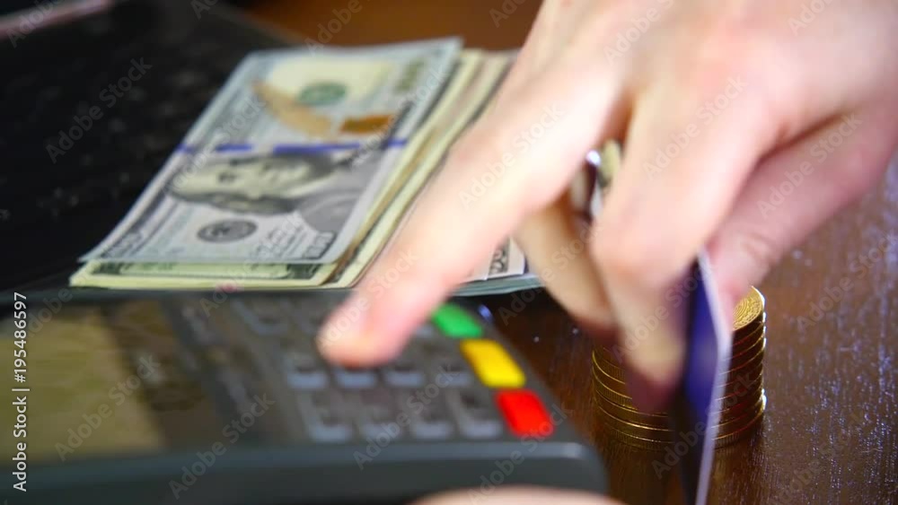 The woman's hand is paid by a bank card using the terminal for payment on the background of gold coins of bitcoins. The concept of a new virtual crypto currency