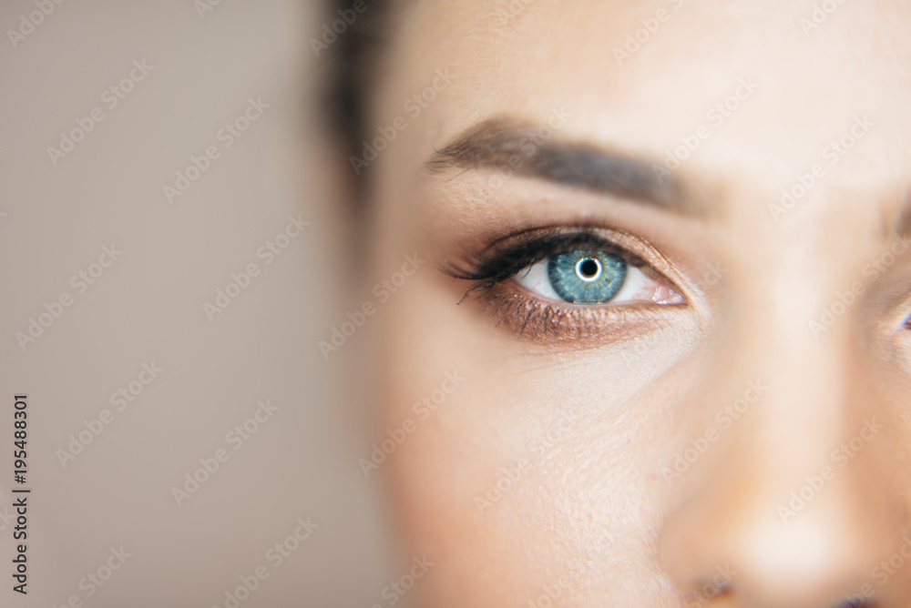 Close-up shot of beautiful blue eye of the attractive fresh woman with natural make-up at beige background. Part of healthy face. - obrazy, fototapety, plakaty 