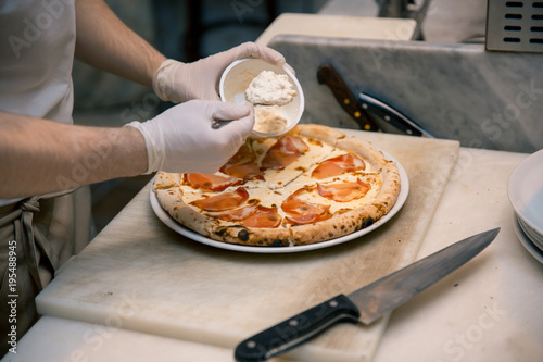 Cook in the kitchen putting the ingredients on the pizza. Pizza concept. Production and delivery of food.