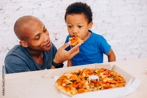 African American father feeding his cute son with pizza. Warm family concept. Warm family, Father and son relationship