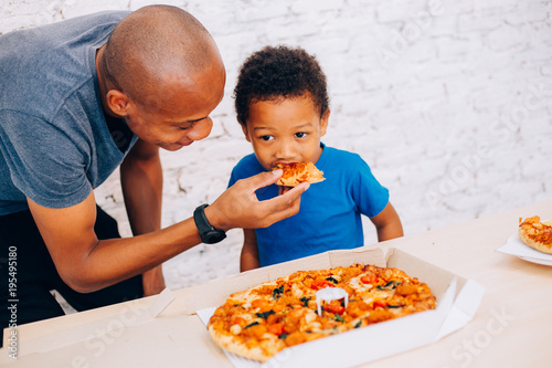 African American father feeding his cute son with pizza. Warm family concept. Warm family, Father and son relationship