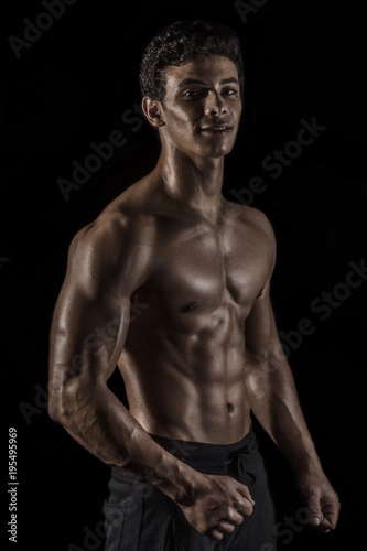 Highly retouched fitness model and bodybuilder. Looking and smile. Posing chest, biceps and six pack abs. Concept of power and self-confidence. black background.