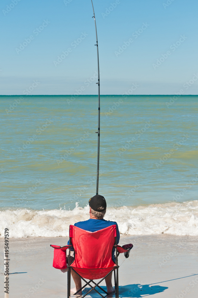 Senior male sitting and surf fishing on a tropical beach Stock Photo
