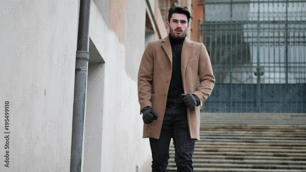 Handsome bearded young man outdoor in winter fashion, walking up marble stairs wearing black turtleneck sweater and woolen blazer jacket in city setting Handsome bearded young man outdoor in winter fashion, walking up marble stairs wearing black turtleneck sweater and woolen blazer jacket in city setting