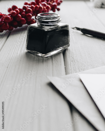 Set of vintage dip pen, inkpot and blank paper sheet on white wooden table with red berries deocration
