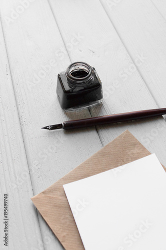 set of vintage dip pen, inkpot and blank paper sheet with envelope on white wooden table