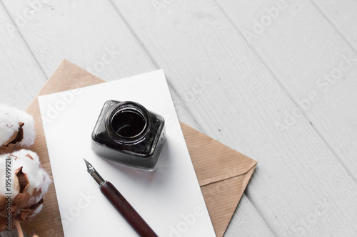 Set of vintage dip pen, inkpot, blank paper sheet, envelope and cotton branch on white wooden tabl