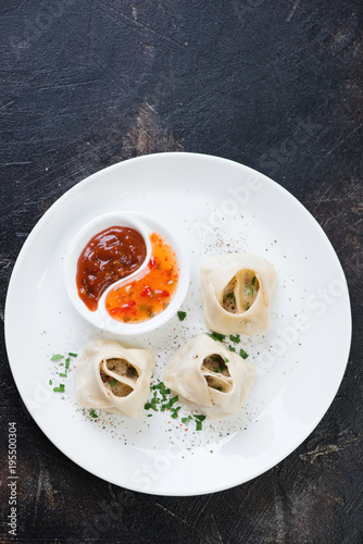 Above view of manti or steamed meat dumplings with sauces, spices and greens served on a white plate, vertical shot with space