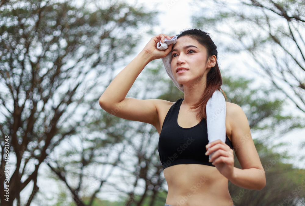 young sporty woman running and wiping her sweat with a towel in park young sporty woman running and wiping her sweat with a towel in park