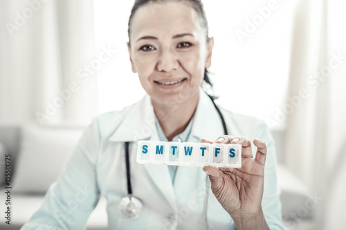 Its for you. Joyful cute pleasant doctor smiling and showing pills holding it in left hand.