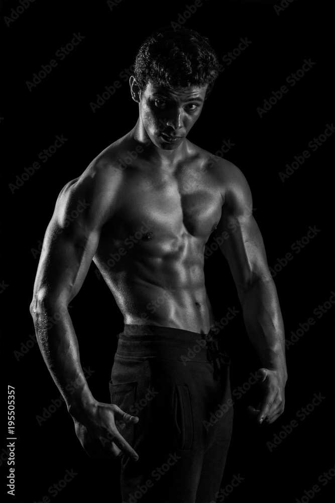 Highly retouched black and white fitness model and bodybuilder, Looking and posing abs and chest. concept of power and strength. black background.
