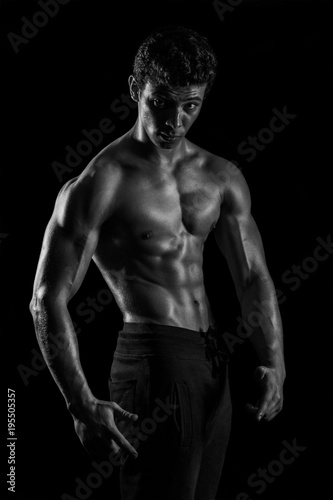 Highly retouched black and white fitness model and bodybuilder, Looking and posing abs and chest. concept of power and strength. black background.