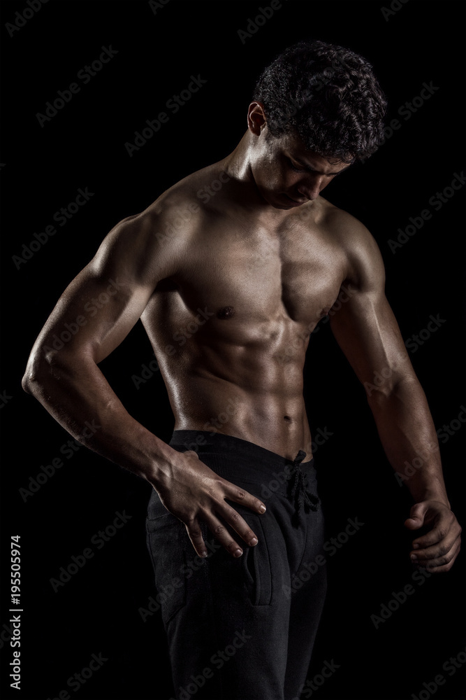 Highly retouched fitness model and bodybuilder. Looking to himself. Posing abs and chest. Concept of power, energy and self-confidence. black background.