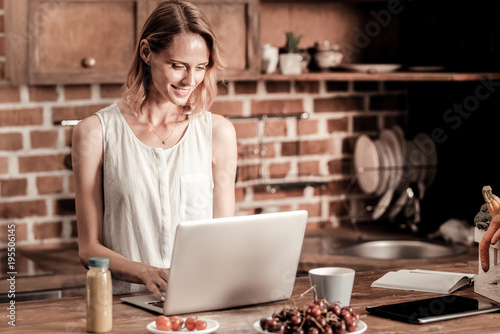 Remote work. Attractive cheerful pleasant woman smiling and looking at the laptop screen while working remotely