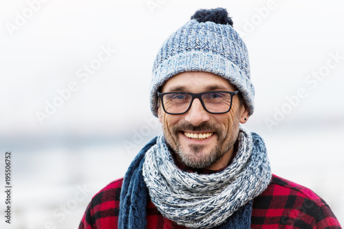 Portrait of smiling urban man in glasses and hat. Happy smiled guy in winter knitted hat and scarf. Smiled man in glasses on white background