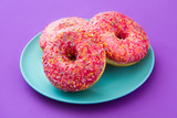 Pink frosted donut with colorful sprinkles on violet background.