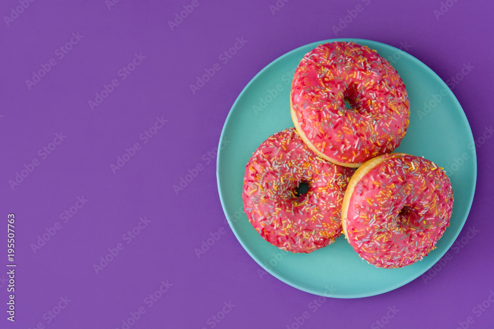 Pink frosted donut with colorful sprinkles on violet background.Top view. Copyspace Pink frosted donut with colorful sprinkles on violet background.Top view. Copyspace