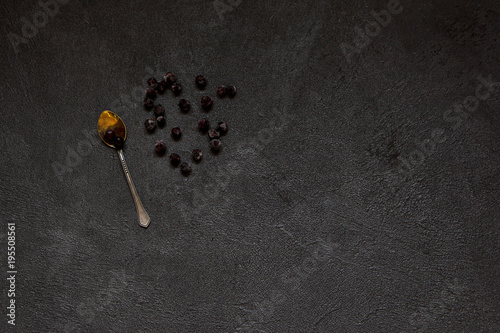  berries black currant and golden spoon on black stone background