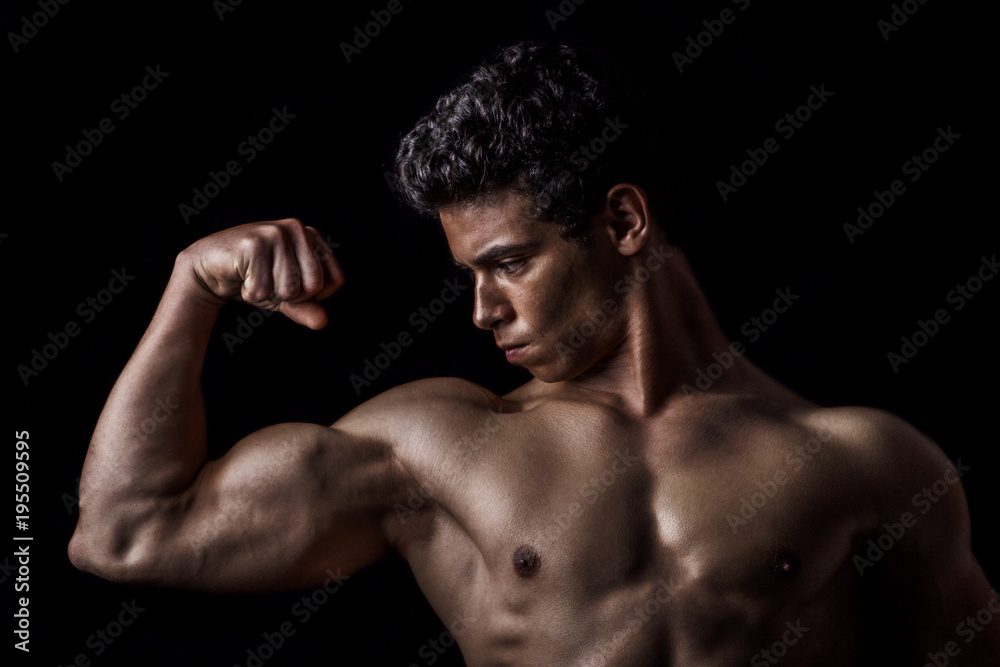 Highly retouched fitness model and bodybuilder posing biceps. concept of strength and power. black background.