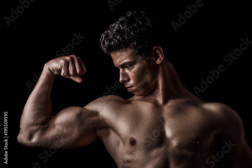 Highly retouched fitness model and bodybuilder posing biceps. concept of strength and power. black background.