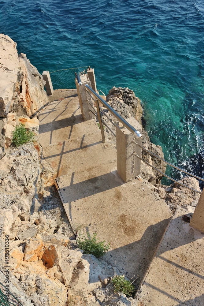 Steep stairs leading down the cliffs to very blue adriatic sea. Dobra Voda, Montenegro, Southeast Europe.