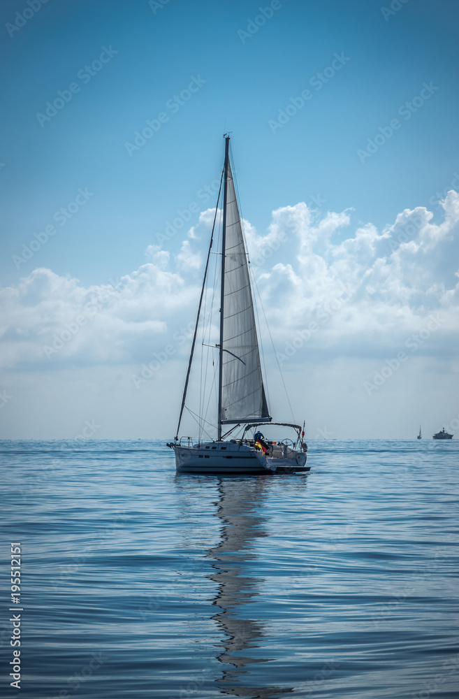 Naklejka premium Sailing boat on the sea sails reflect on a calm water summer day dark blue colors
