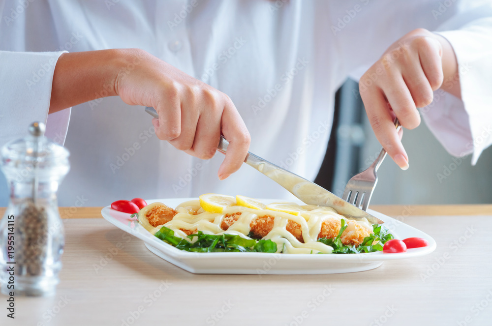 Woman hands cutting and eating delicious meal with knife and fork at restaurant.