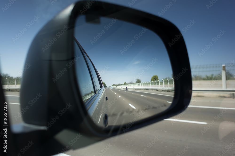 Reflection seen through car side mirror - two-lane winding road with twilight sky and sunset. Arabian desert between dubai and abu dhabi