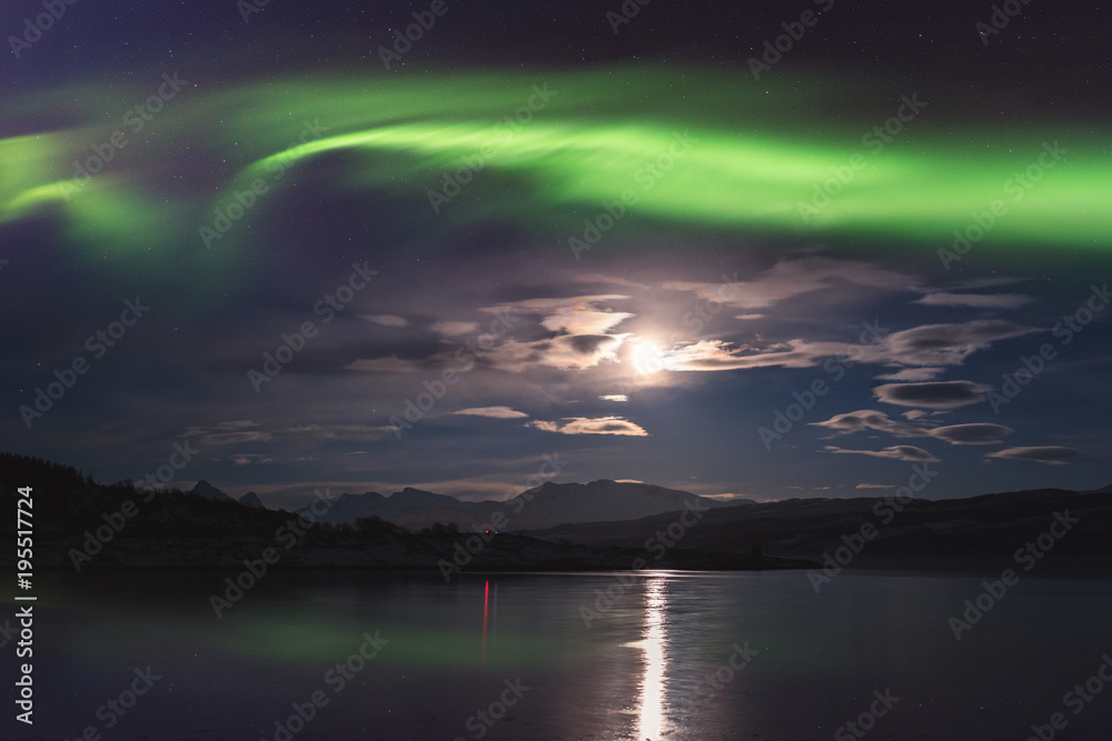 Northern lights (aurora borealis) in Lofoten islands, Norway. Amazing night winter landscape with polar lights, starry sky with full moon and reflection in the water