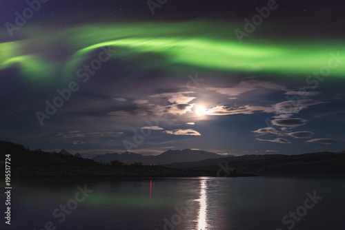 Northern lights (aurora borealis) in Lofoten islands, Norway. Amazing night winter landscape with polar lights, starry sky with full moon and reflection in the water