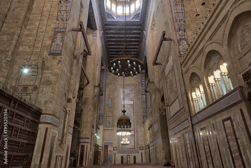 Interior of al Refai mosque with old decorated bricks stone wall, colored marble decorations, wooden ornate ceiling, big brass chandeliers, and wooden latticework door, Cairo, Egypt