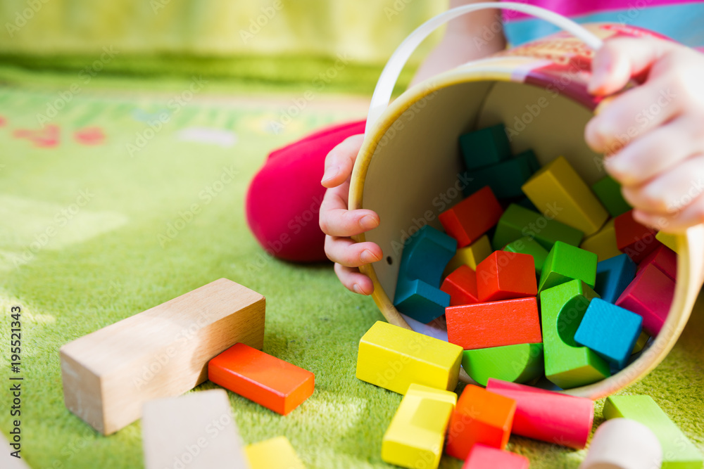 Naklejka premium Small child playing with wooden blocks on green carpet