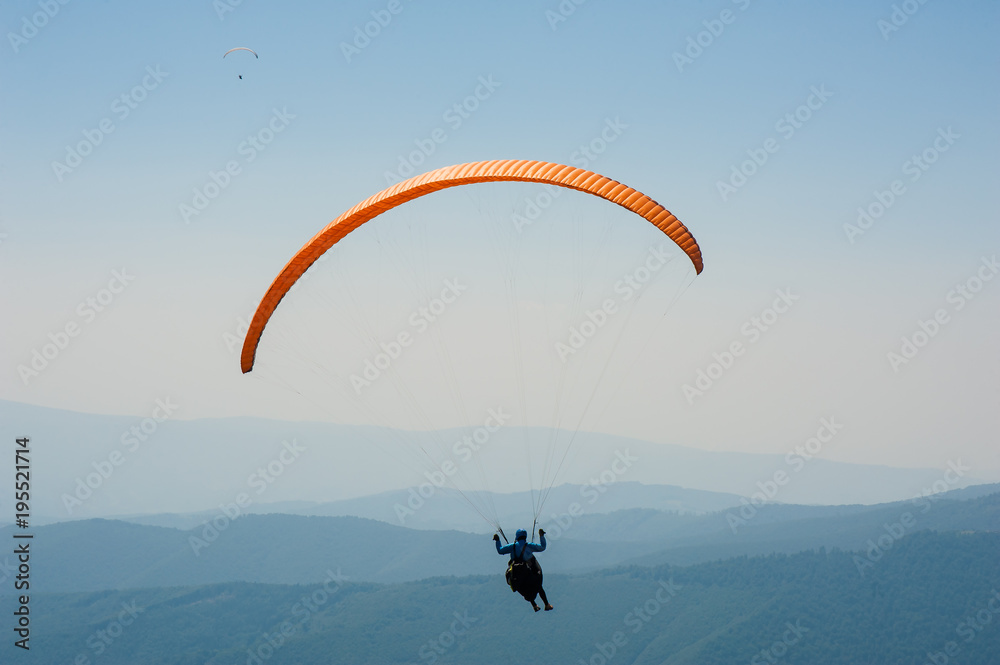 Paraglider flies over a mountain valley on a sunny summer day. Paragliding in the Carpathians in the summer. Paraglider flies over a mountain valley on a sunny summer day. Paragliding in the Carpathians in the summer.