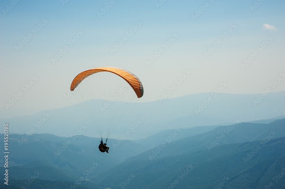 Paraglider flies over a mountain valley on a sunny summer day. Paragliding in the Carpathians in the summer. Paraglider flies over a mountain valley on a sunny summer day. Paragliding in the Carpathians in the summer.