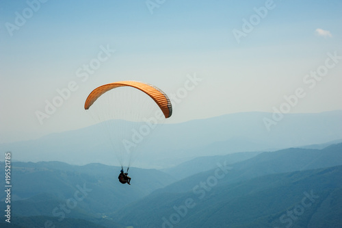 Paraglider flies over a mountain valley on a sunny summer day. Paragliding in the Carpathians in the summer.