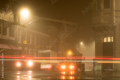 night scene with traffic passing by parked vehicles and crane in background removing Christmas lights