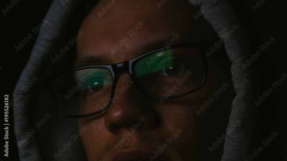 Programmer with glasses and a hood works at a computer in the dark, a reflection in glasses close-up, 4k Programmer with glasses and a hood works at a computer in the dark, a reflection in glasses close-up, 4k