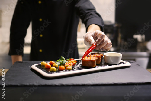 Chef preparing delicious grilled salmon wrapped in bacon and vegetable salsa for serving in restaurant