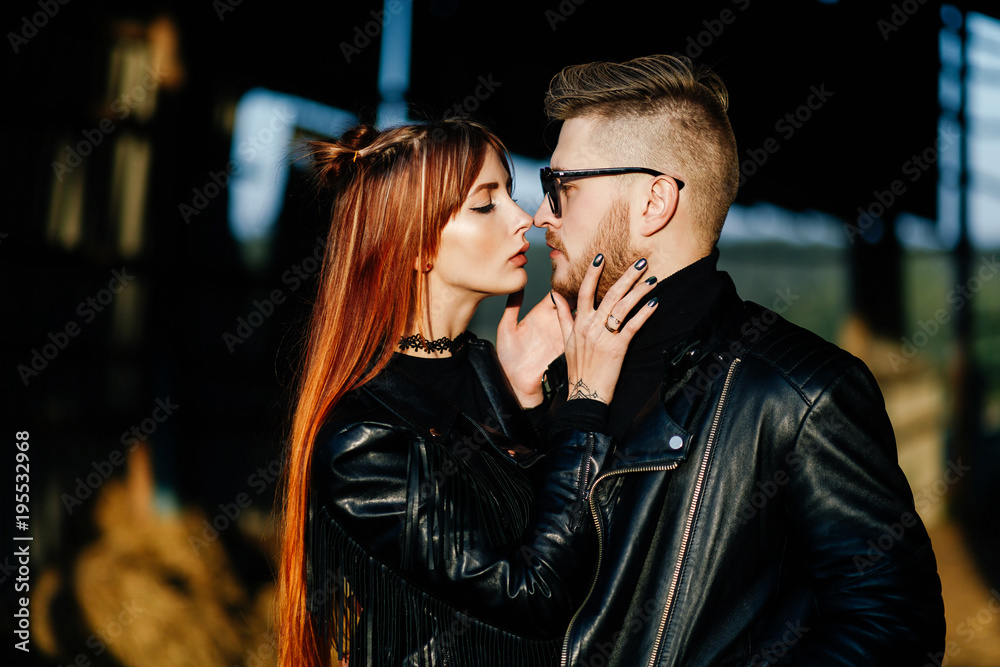 bearded guy hugging with a red-haired girl at sunset. Loving Couple dressed in leather jackets