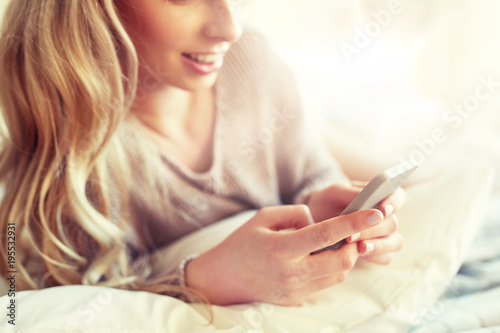 close up of woman with smartphone in bed at home