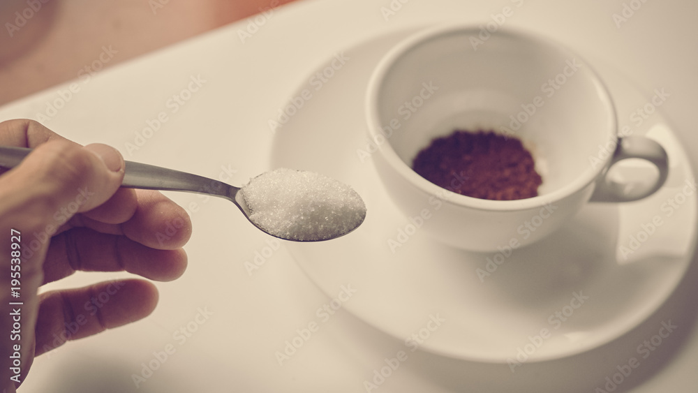 Closeup of hand pouring sugar from spoon in cup with coffee, image with warm vintage toning Closeup of hand pouring sugar from spoon in cup with coffee, image with warm vintage toning