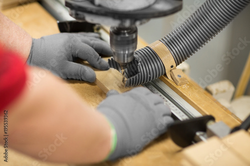 carpenter with drill press and board at workshop © Syda Productions