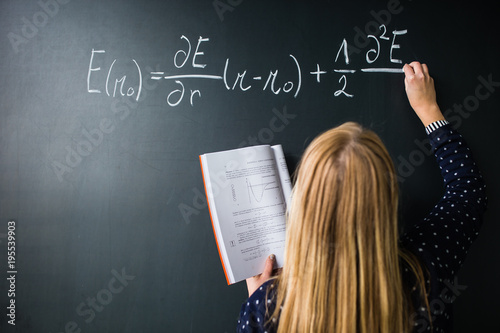 Pretty, young college student writing on the chalkboard/blackboard during a math class (colort toned image; shallow DOF) photo