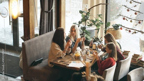 Four beautiful women sit in cafe with phones