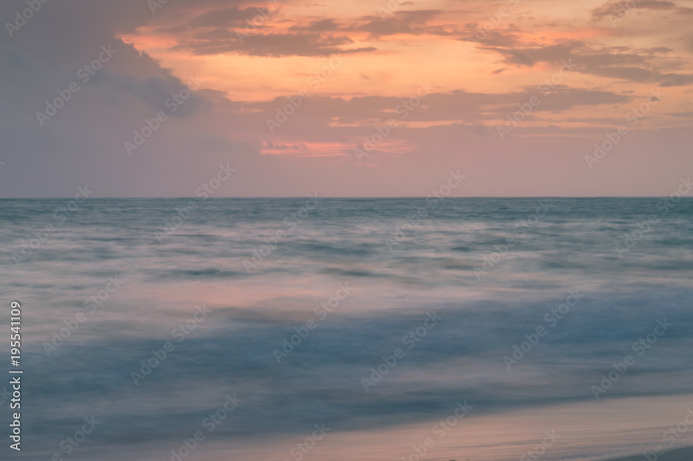 A long exposure of the sea at golden hour, as dawn starts to break over a white sandy beach.