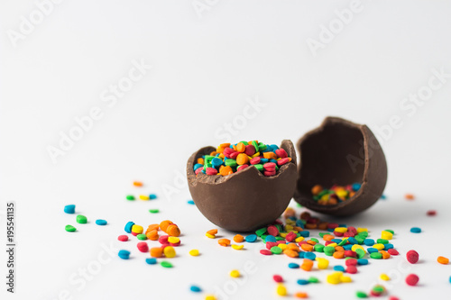 Broken Chocolate Easter egg with multi-colored candy decorations on a white background. Copy space