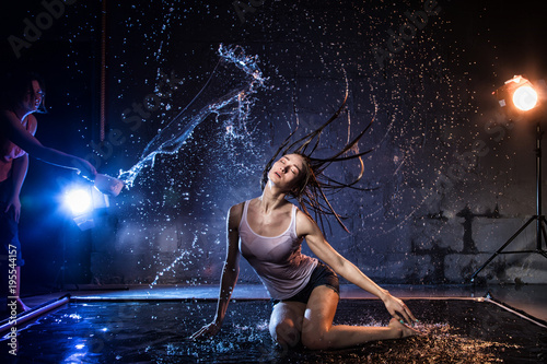 Girl with long hair during photoshoot with water in photo studio and woman who pours water on her