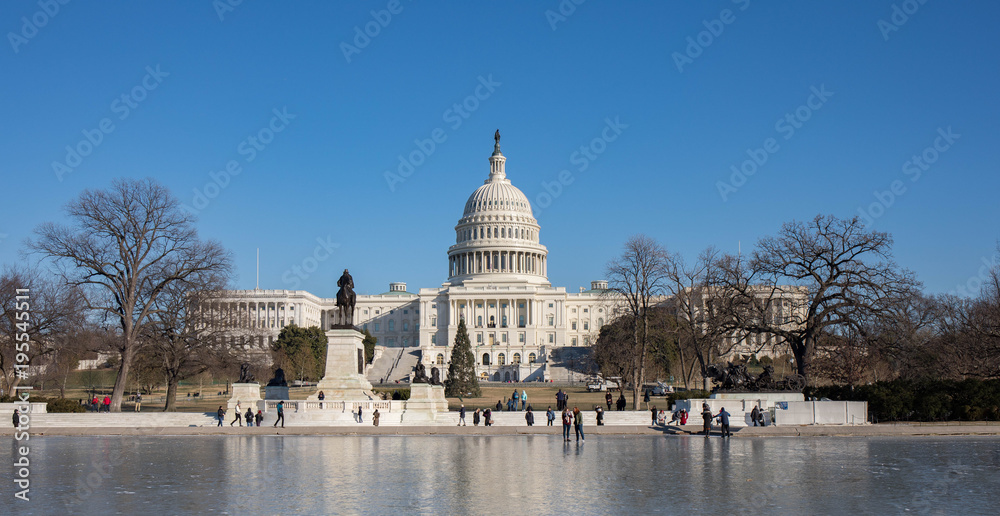 The Capitol Building in Washington, D.C. in the winter and the reflection pool is frozen with tourists walking on it.