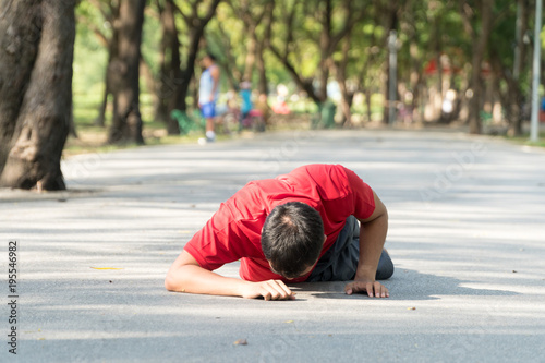 Young men wearing red shirts falling down to the pavement in public park while jogging. Concept injury from exercise.
