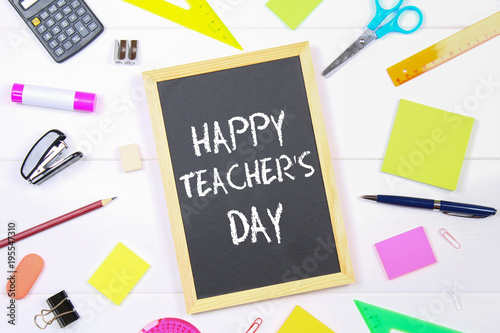 Text chalk on a chalkboard: Happy Teacher's Day. School supplies, office, books, apple.